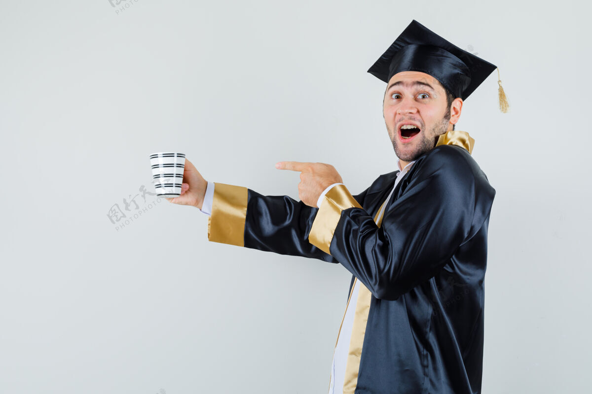 成年人年轻人指着一杯毕业生制服的饮料 看上去很高兴制服肖像年轻