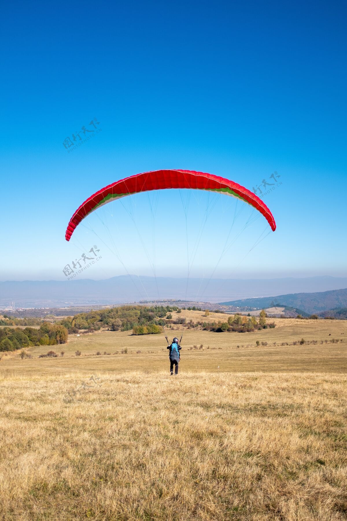 活动一个人手持红色降落伞在蓝天下飞翔的垂直画面 周围绿树成荫行动翅膀危险