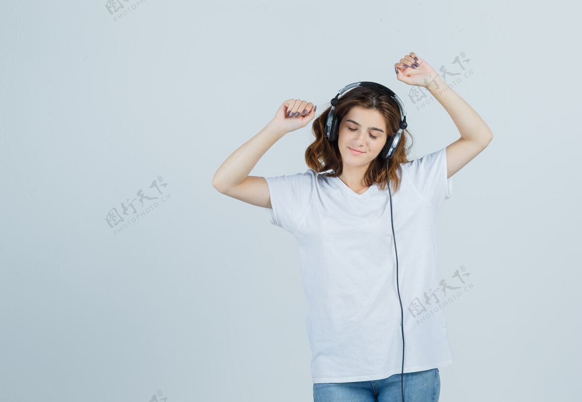 女孩身着白色t恤 牛仔裤 戴着耳机欣赏音乐的年轻女性的肖像 看上去很快乐人模型乐趣