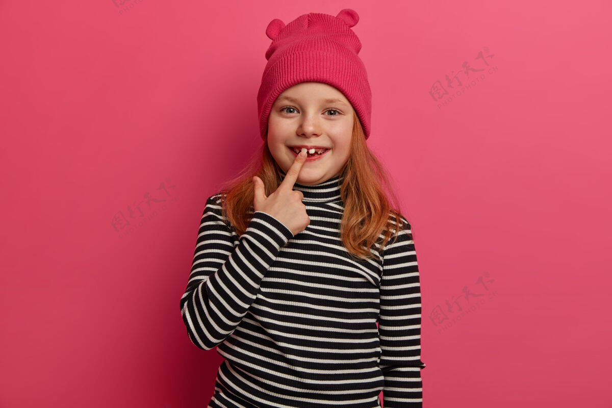 童年这张照片是一个小孩喜获新生的成人牙齿 姜黄色头发 穿着条纹毛衣 戴着时髦的帽子 在玫瑰色的墙上摆出迷人的正面表情看看我洁白的牙齿高兴冷显示