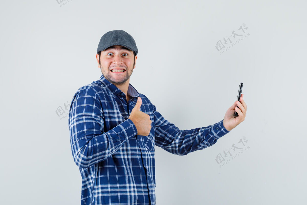 自信年轻人在衬衫 帽子上打视频电话时竖起大拇指 看上去很高兴 正前方男人欢呼前面