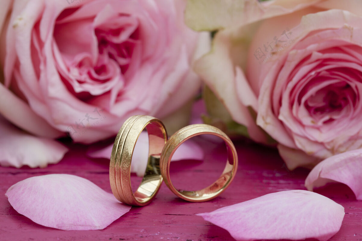 新郎桌上放着漂亮的粉红玫瑰的订婚戒指特写镜头金色绿色戒指