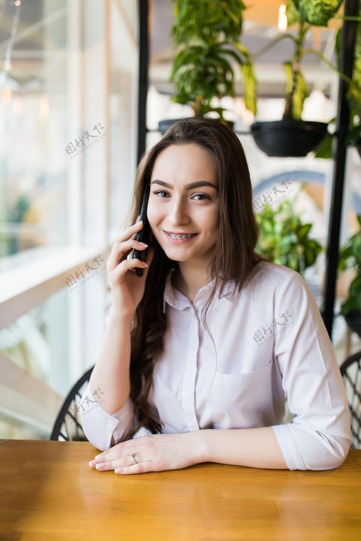 设备年轻迷人的女人闲暇时独自坐在咖啡厅打电话 迷人的女人微笑着在咖啡厅休息时用手机聊天桌子当代女士