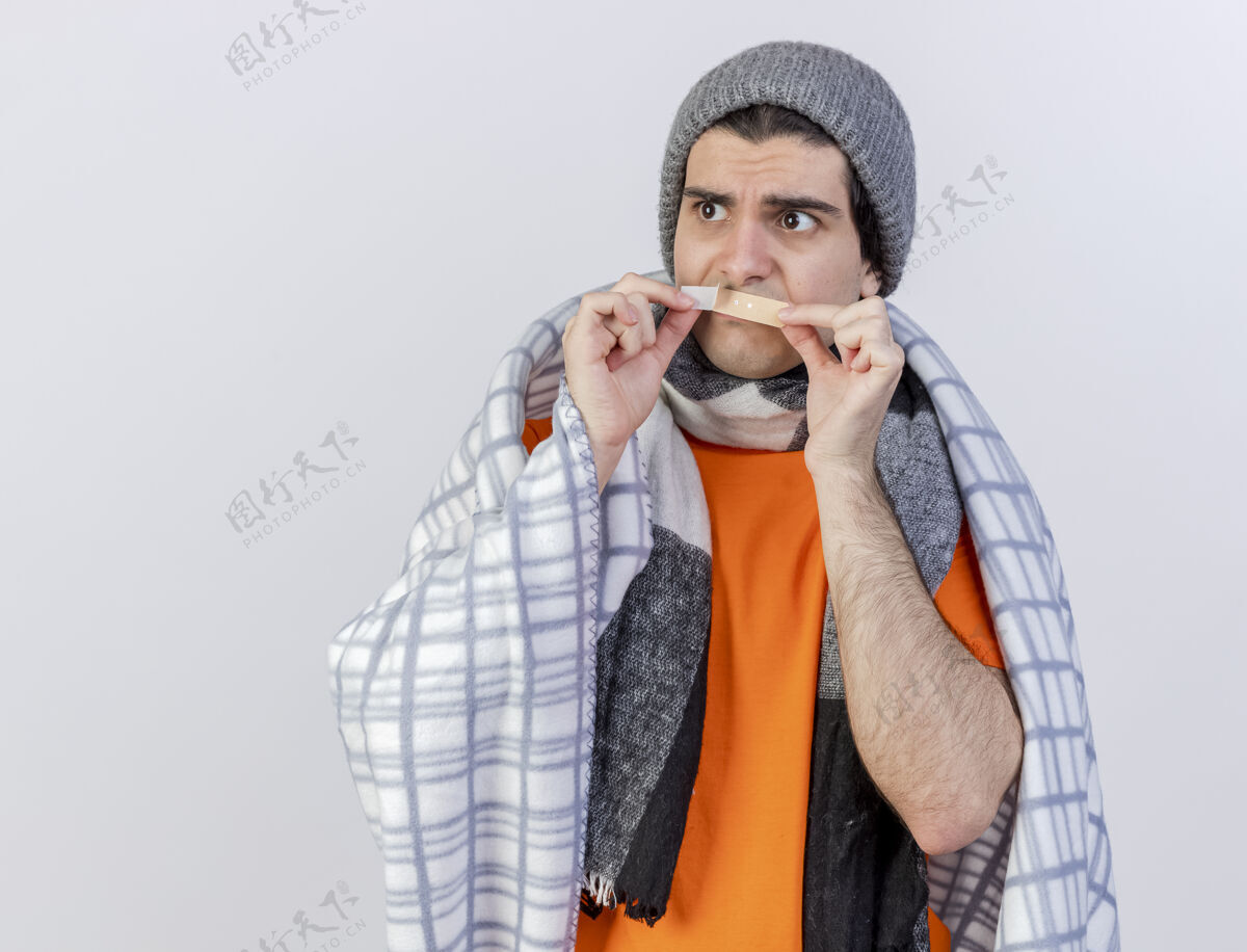 嘴巴望着旁边一个戴着冬天帽子 披着方格围巾 嘴上贴着膏药的年轻病患 隔离在白色的背景上包装围巾疾病