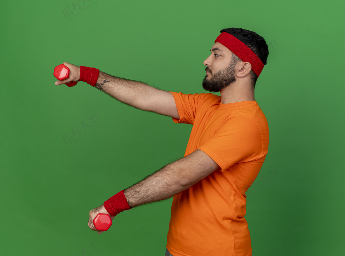 腕带站在侧视图年轻的运动男子戴着头带和腕带锻炼与哑铃隔离在绿色背景运动哑铃头带