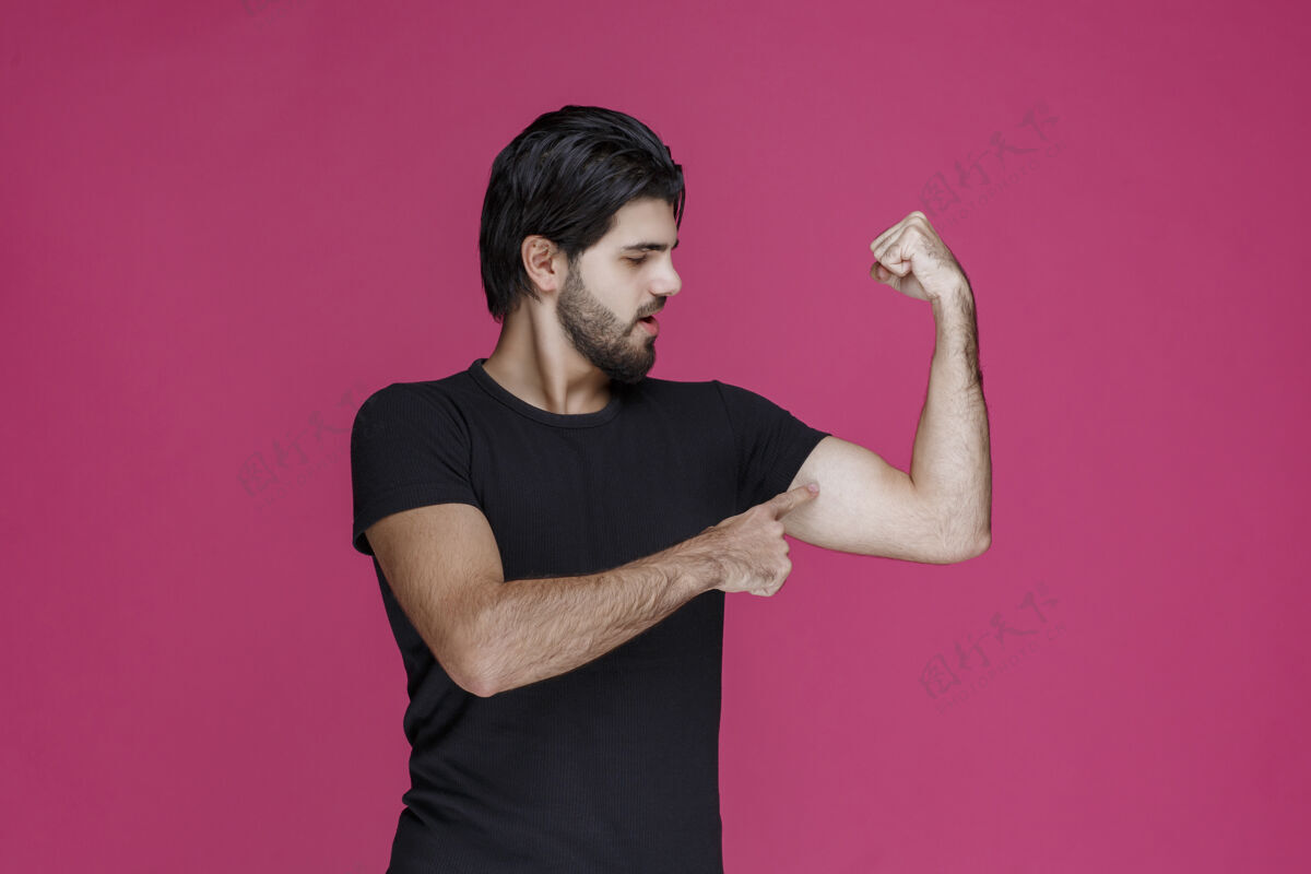 年轻人穿黑衬衫的男人露出他的手臂肌肉姿势斗士男性