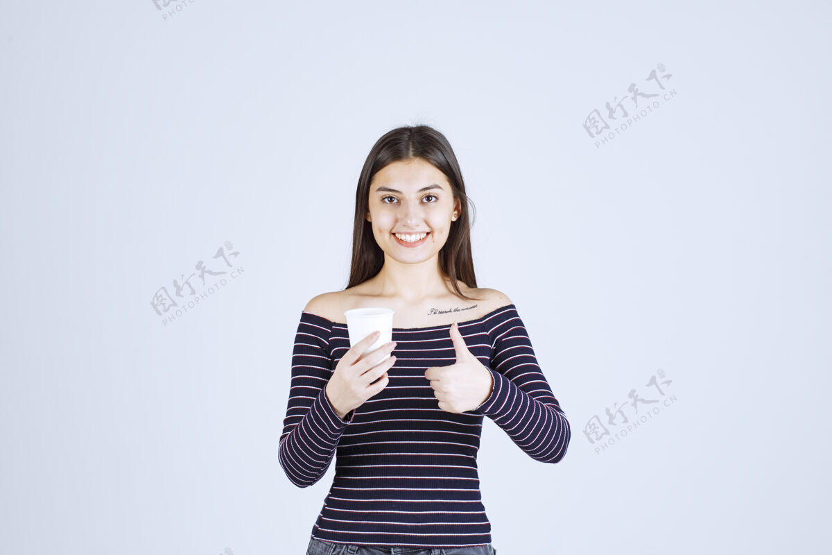 女人穿着条纹衬衫的女孩拿着一个塑料咖啡杯 指着一个好味道成人服装积极