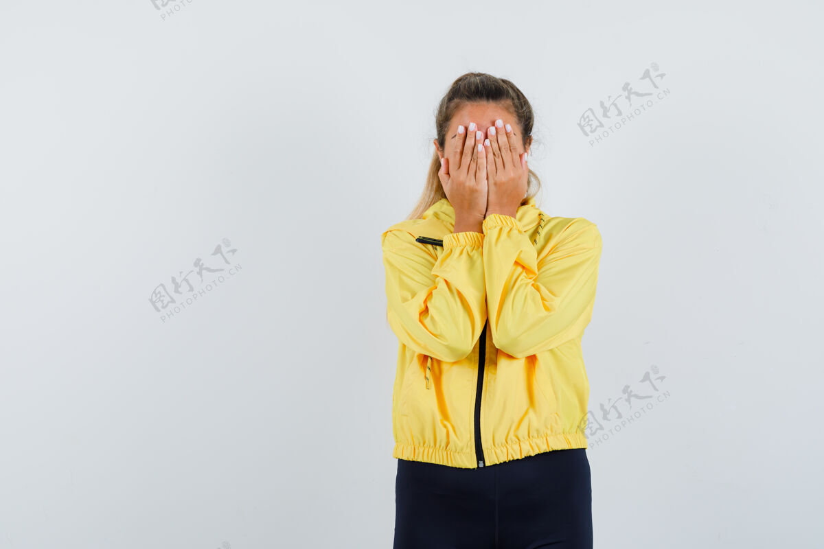 女性一个金发碧眼的女人用手捂住脸 穿着黄色棒球服和黑色裤子 看起来很胆小自然头发夹克
