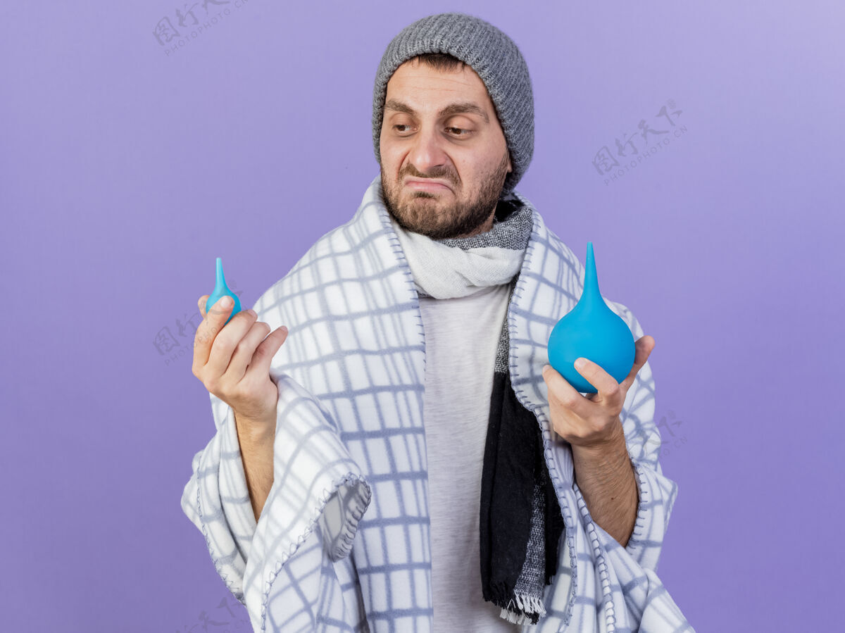 悲伤悲伤的年轻病人戴着冬天的帽子 戴着围巾 看着紫色背景上孤立的灌肠年轻生病围巾