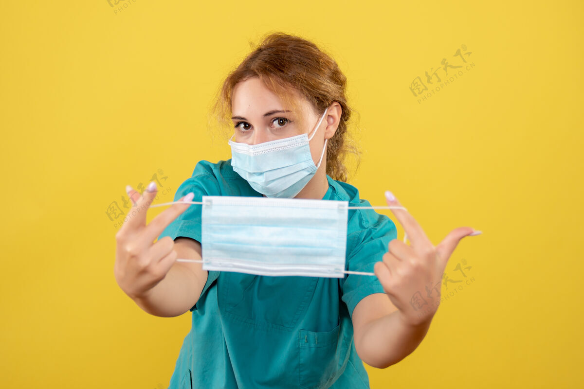 另一个正面图女医生穿着医用衬衫戴着口罩 手持另一个口罩 彩色covid-19病毒健康情绪大流行微笑成人黄色