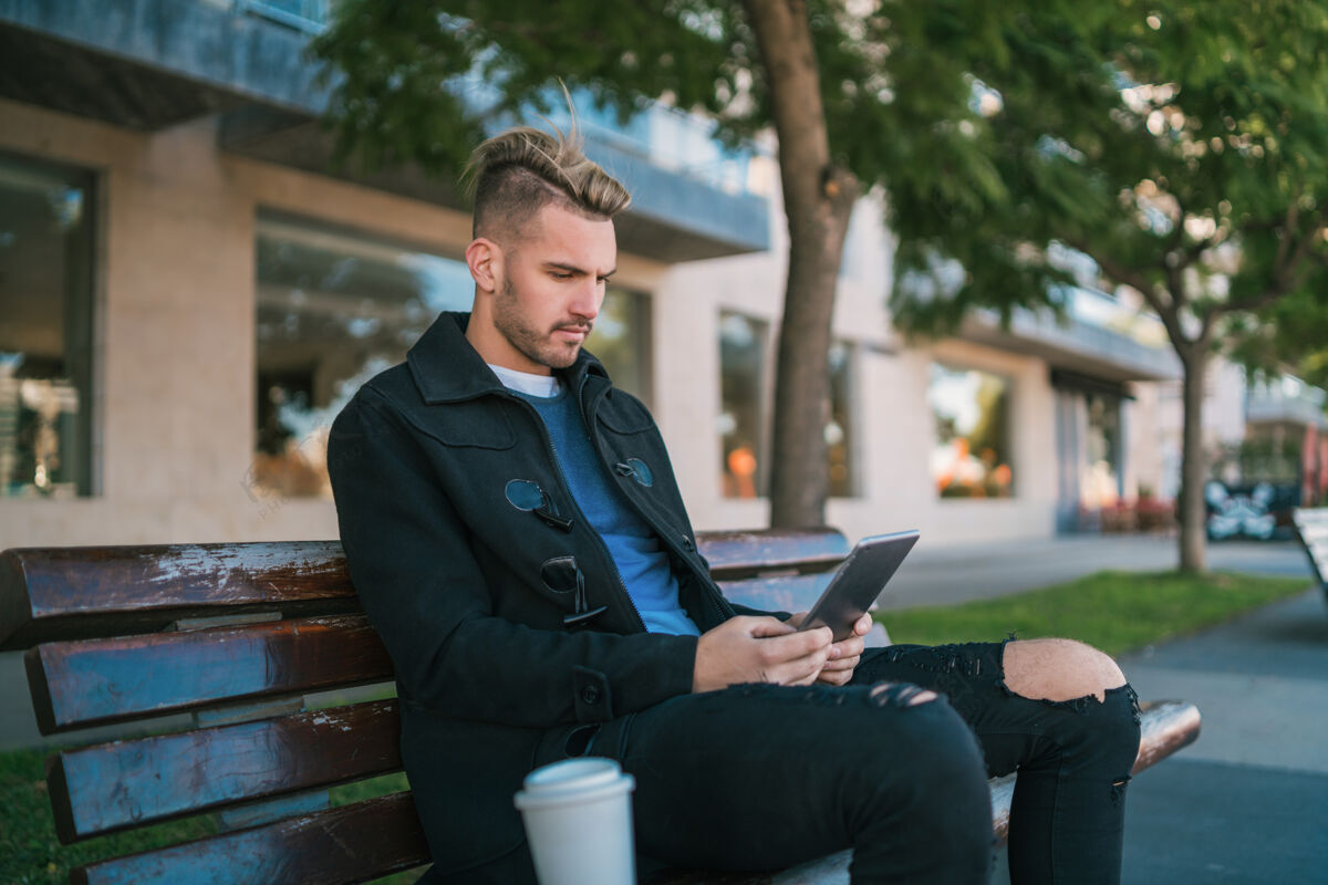 城市年轻帅哥坐在长凳上在户外使用数码平板电脑的照片人移动成人