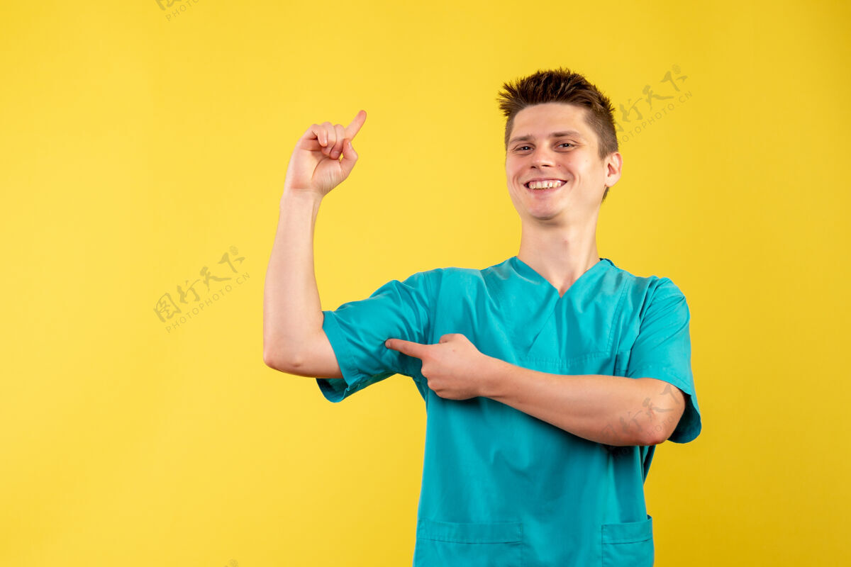 成人黄色墙壁上穿着医疗服的男医生的正视图健康男人人
