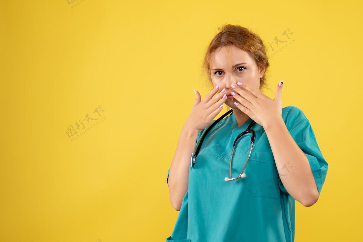 病毒黄色墙壁上穿着带听诊器的医疗服的女医生的正视图人正面口哨