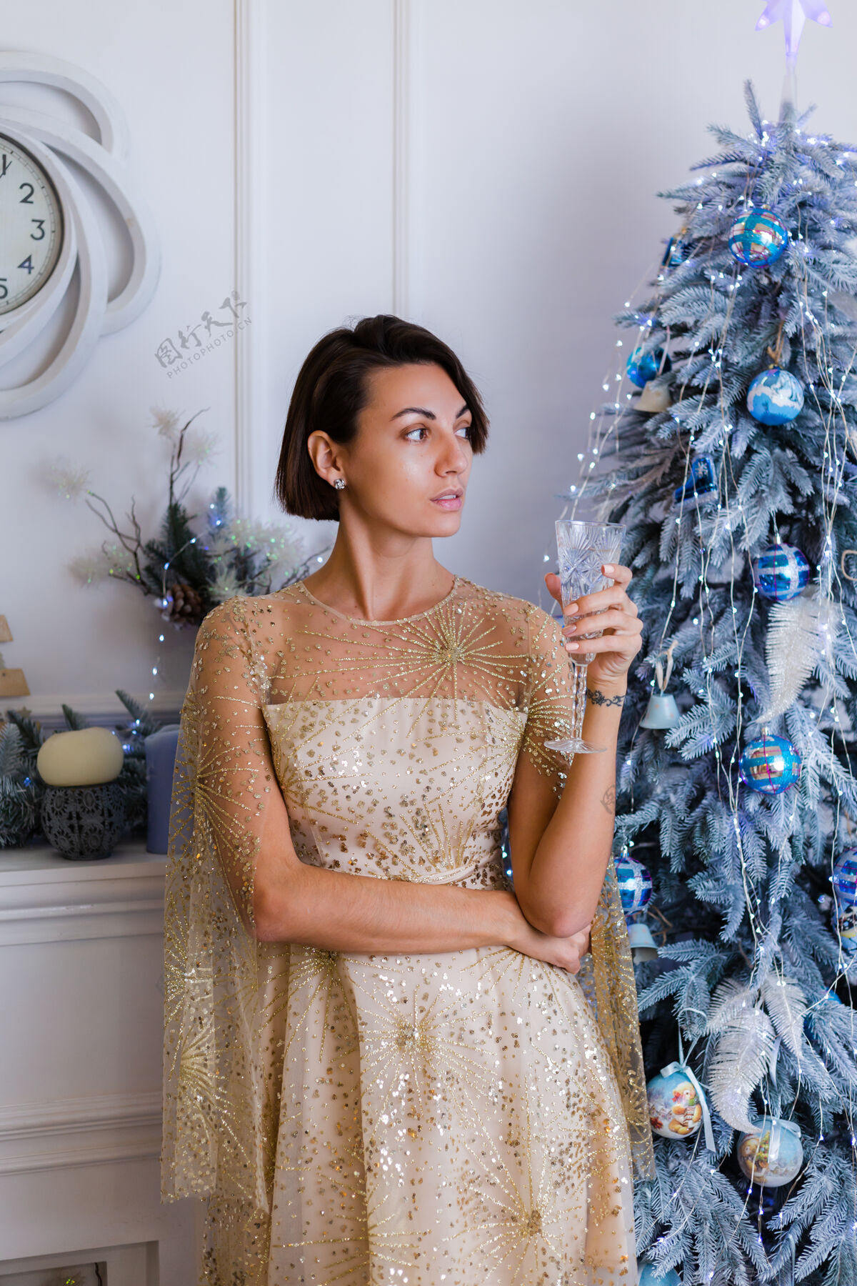 十二月一个穿着闪亮的金色圣诞晚礼服的女人在家里拿着一杯香槟在圣诞树旁女性性感漂亮