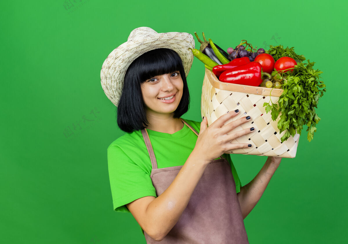 帽子身着制服的年轻女园丁微笑着戴着园艺帽 手里拿着菜篮微笑绿色空间