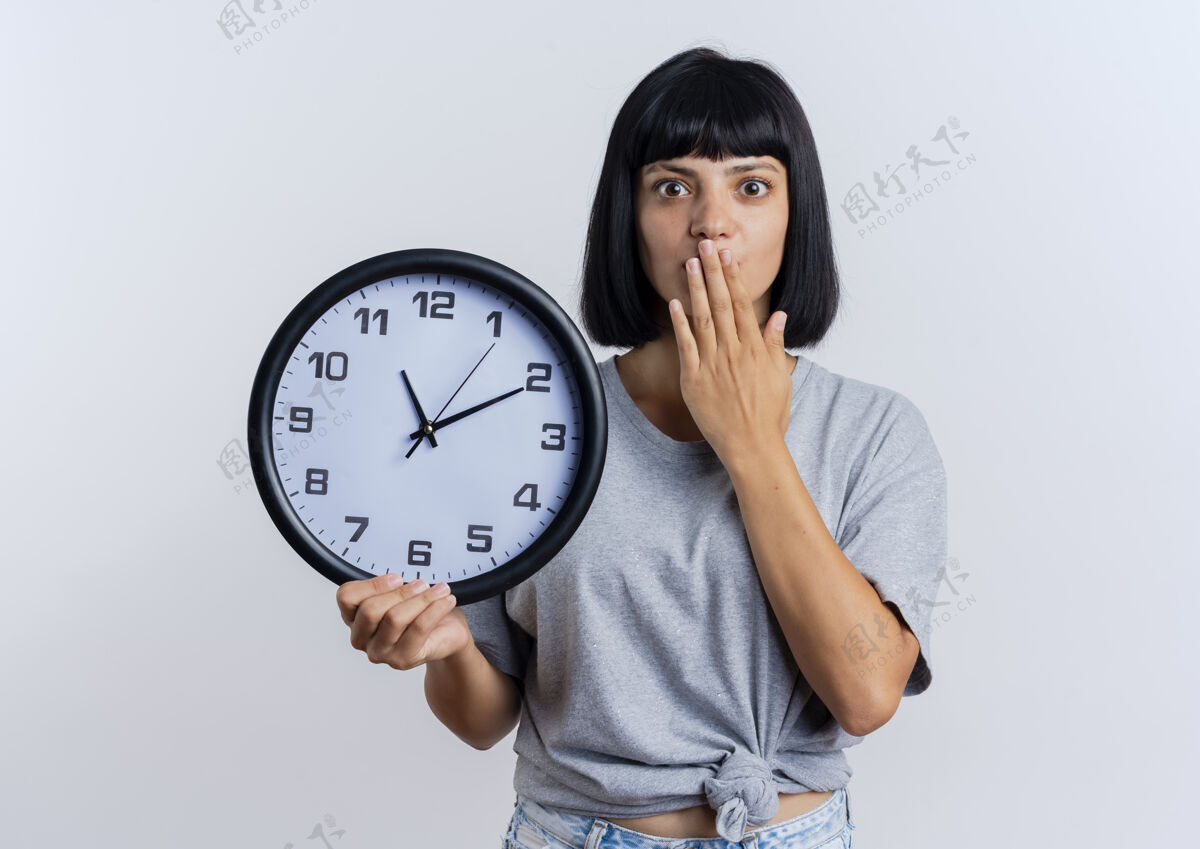 女孩震惊的年轻黑发白人女孩把手放在嘴里拿着钟复制时钟拿着