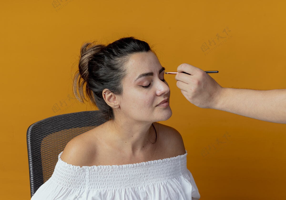有人有人在化妆台上用化妆刷涂抹眼影 坐在桌子上的化妆工具被隔离在橙色的墙上刷子桌子申请