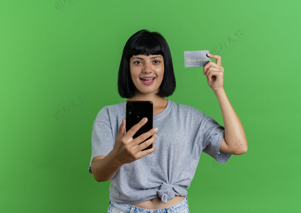 女孩快乐的年轻黑发白人女孩持有信用卡和电话举行信用黑发