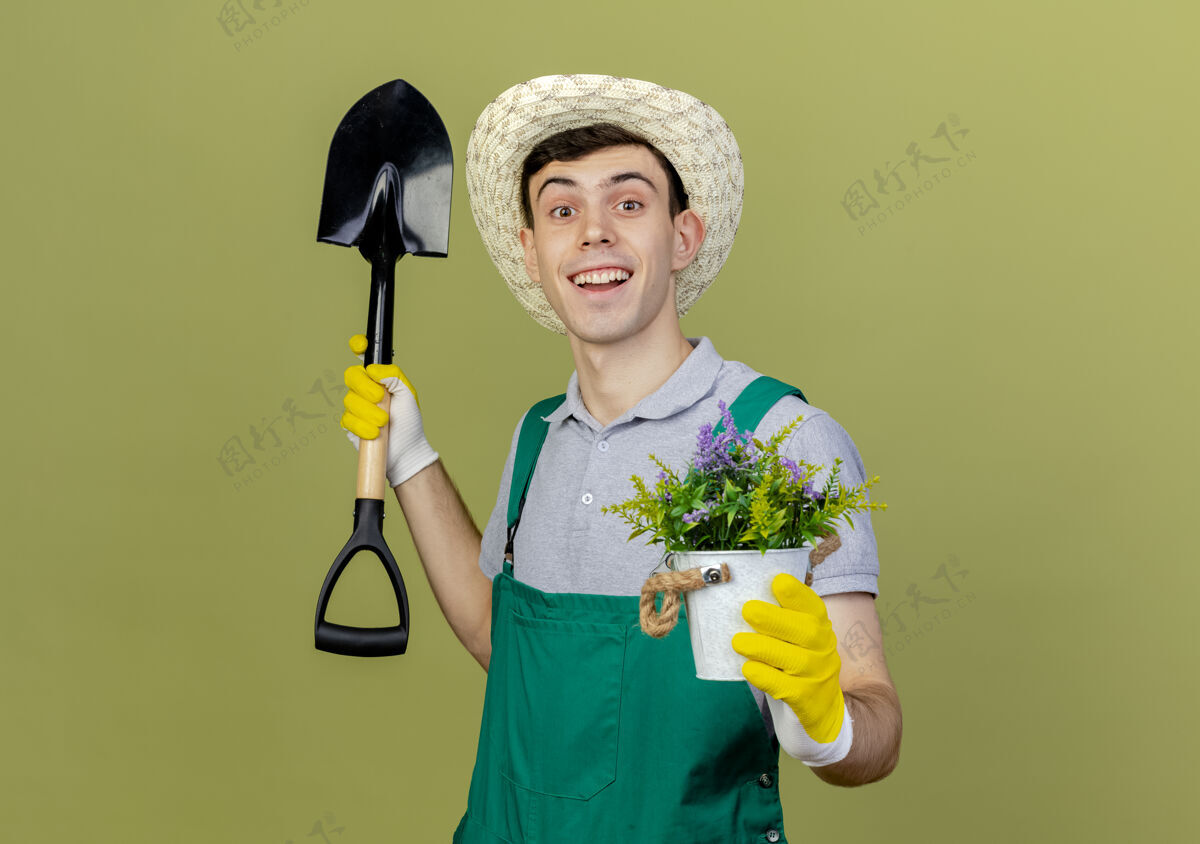 花园兴奋的年轻男园丁戴着园艺帽和手套在花盆里拿着铲子和花园艺空间复制