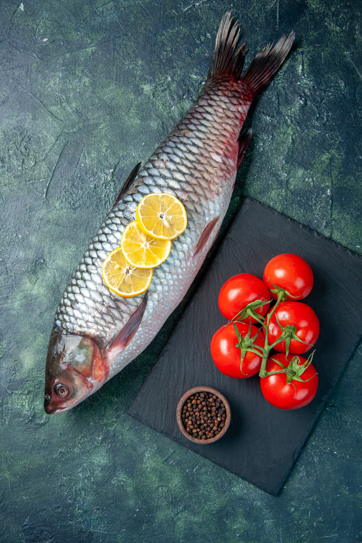 肉在深蓝色的背景上俯瞰新鲜的生鱼片和西红柿水平海鲜餐