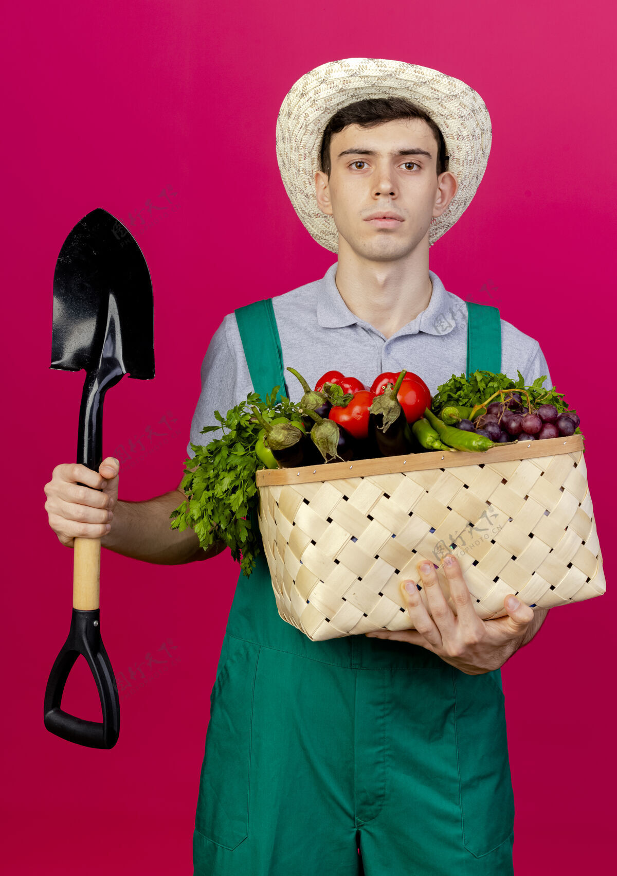 粉红色自信的年轻男园丁戴着园艺帽 手里拿着菜篮和铲子蔬菜持有空间