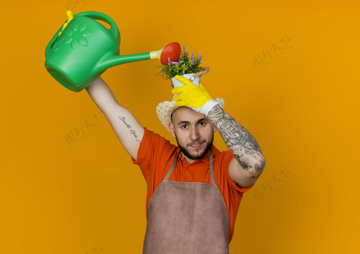 复制微笑的男园丁戴着园艺帽 头顶花盆 假装用水壶浇水水持有花盆