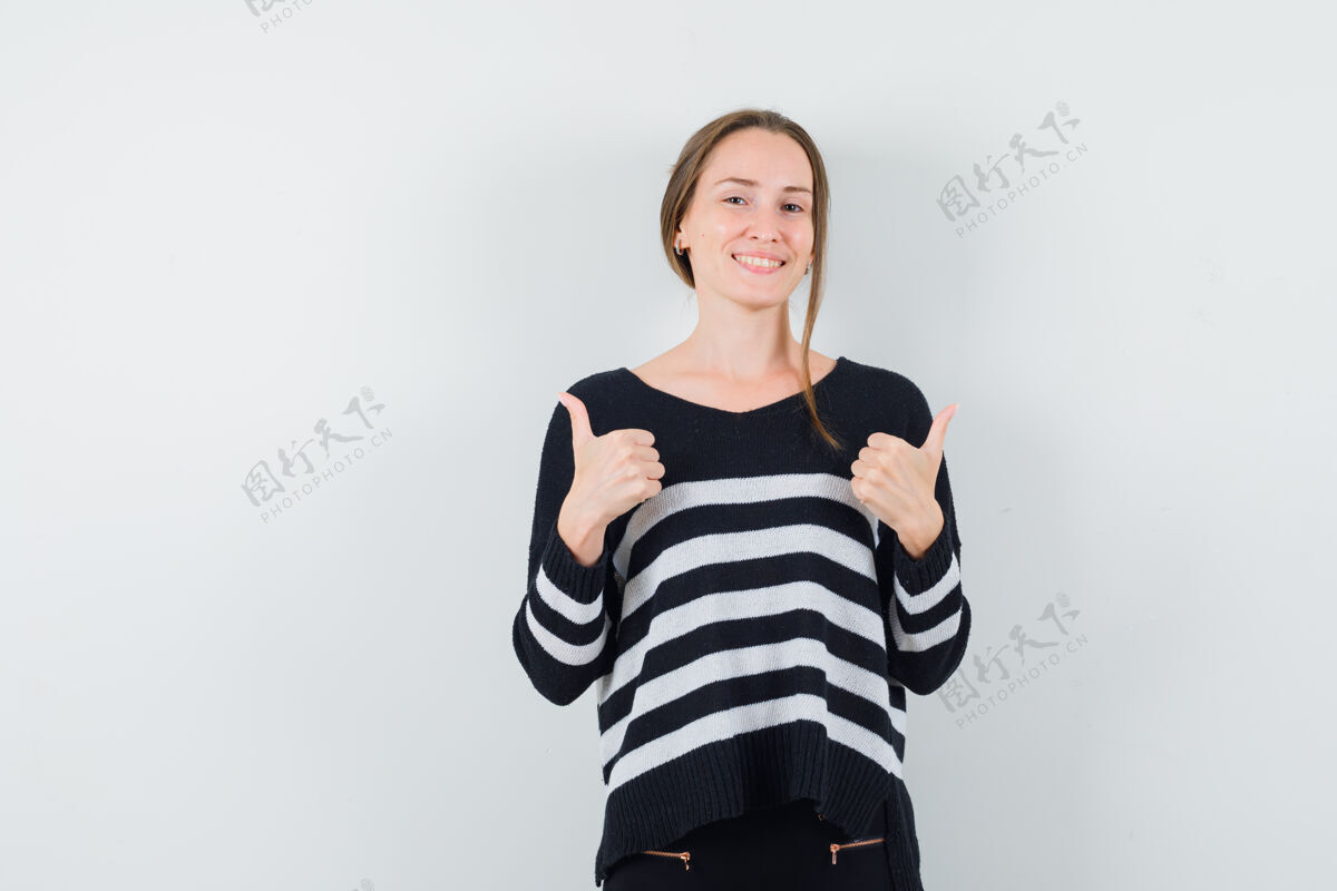 漂亮穿着条纹针织衫和黑色裤子的年轻女子竖起大拇指 看起来很开心亚洲人干净前面