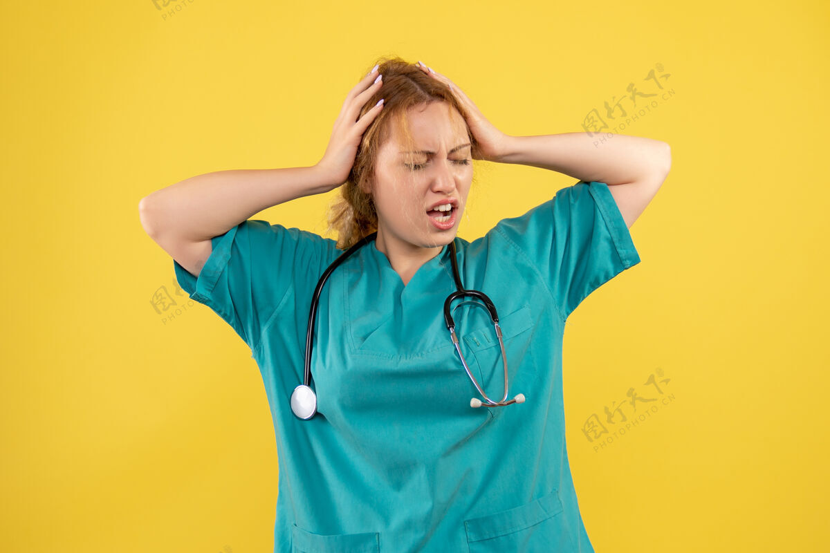 病毒黄色墙壁上穿着带听诊器的医疗服的女医生的正视图正面医疗器械医生