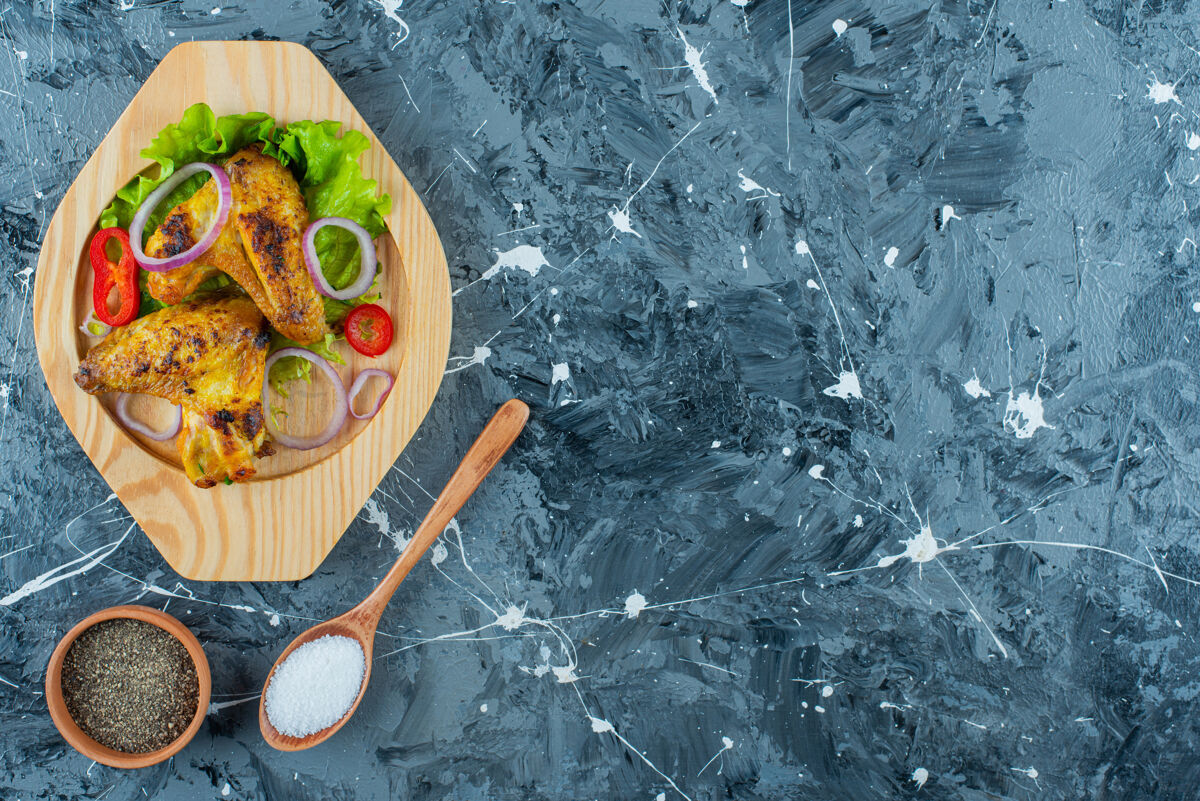 新鲜把烤鸡翅和蔬菜放在木制盘子里 蓝色背景勺子生菜碗