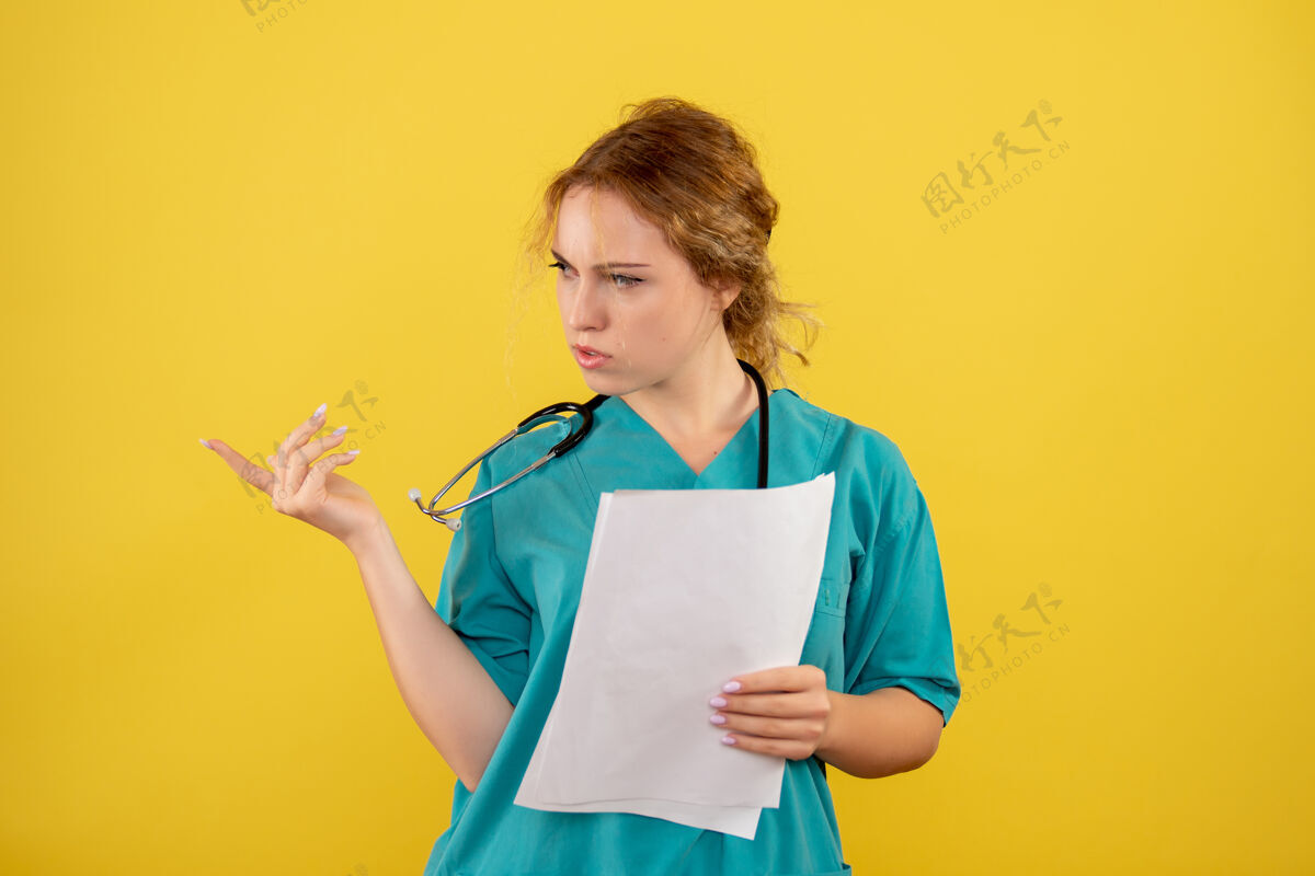 护士黄墙上穿着医疗服的女医生手持分析图肖像微笑听诊器