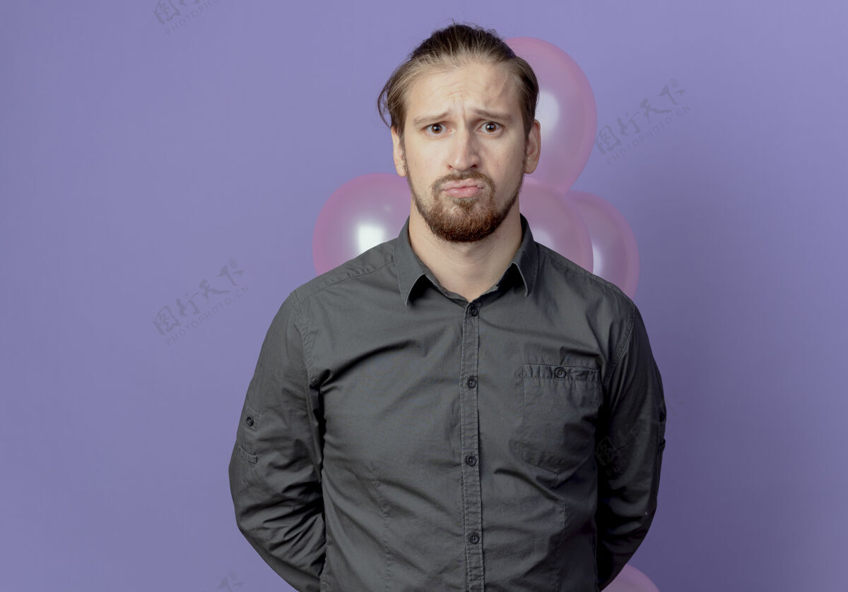 氦心烦意乱的帅哥身后拿着氦气球 在紫色的墙上显得孤立无援紫色气球心烦意乱