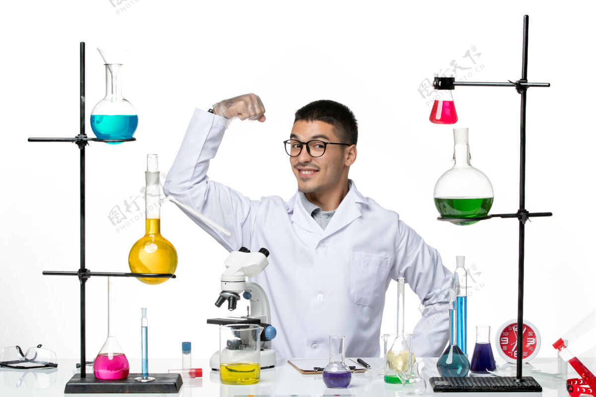 专业正面图穿着白色医疗服的男性化学家坐在白色背景的柯维氏病病毒科学实验室里 拿着解决方案和弯曲的身体容器科学医学