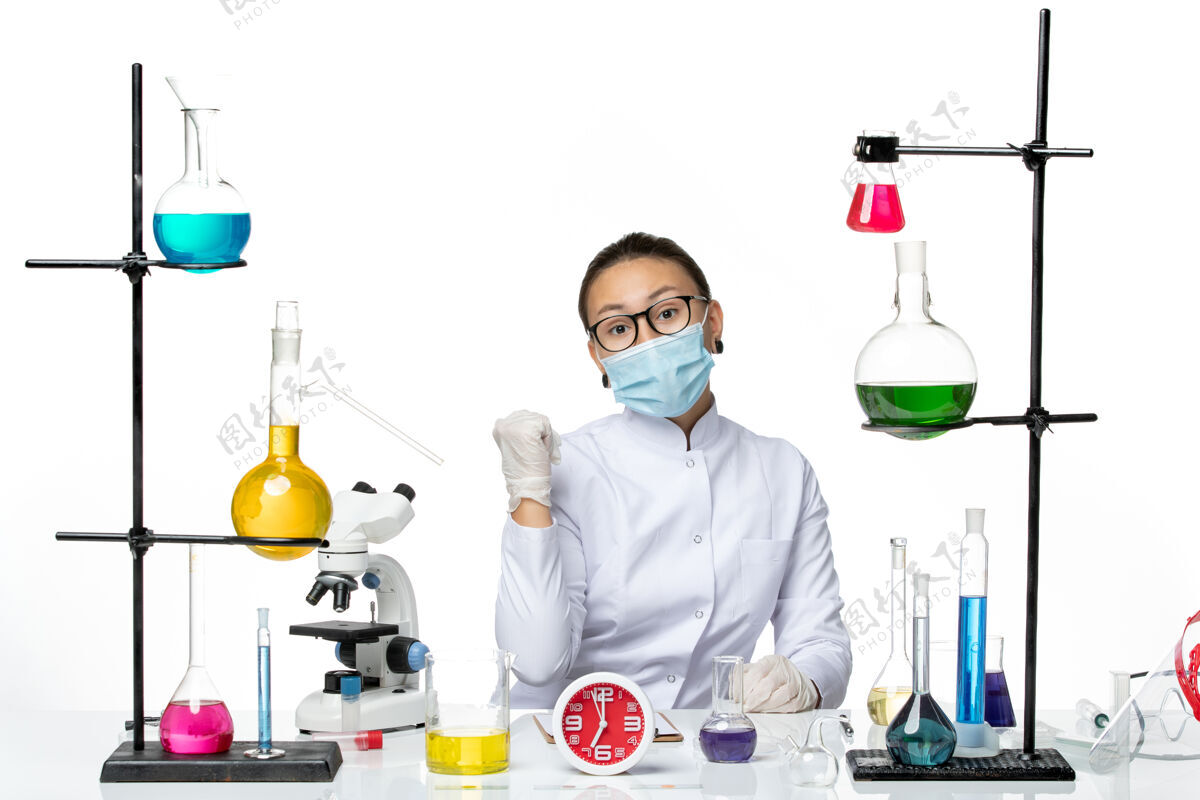 视图前视图穿着白色医疗服的女化学家带着面罩坐在白色背景上的解决方案欣喜若狂化学家病毒covid-splash实验室病毒医生面具