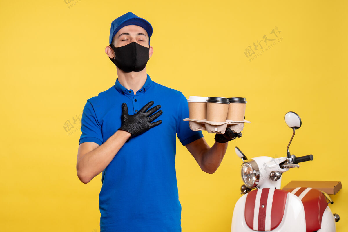 咖啡正面图戴面具的男信使拿着咖啡在黄色工作服上-大流行服务递送工作送货手持人