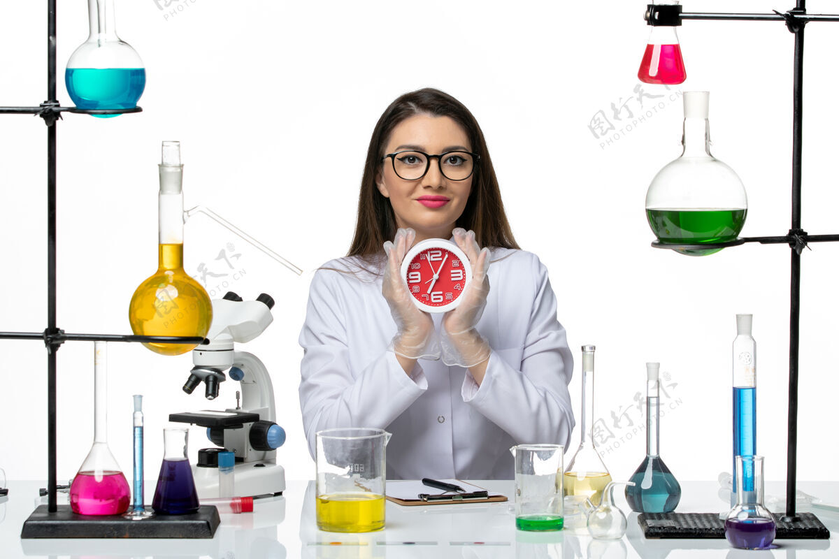 大流行前视图穿着白色医疗服的女化学家拿着白色背景上的时钟科学病毒实验室病毒-大流行时钟微笑工作