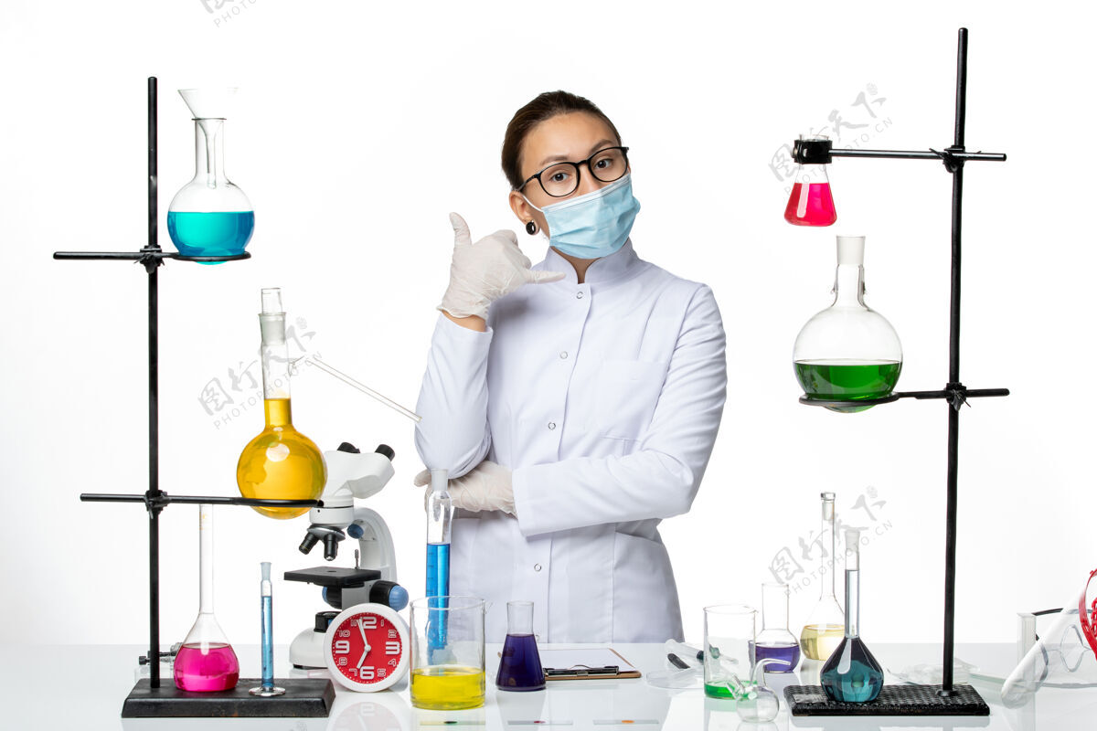 化学前视图：身穿医疗服的女化学家 戴着口罩 站在房间里 白色背景上的溶液病毒化学实验室covid-splash病毒药品喷溅