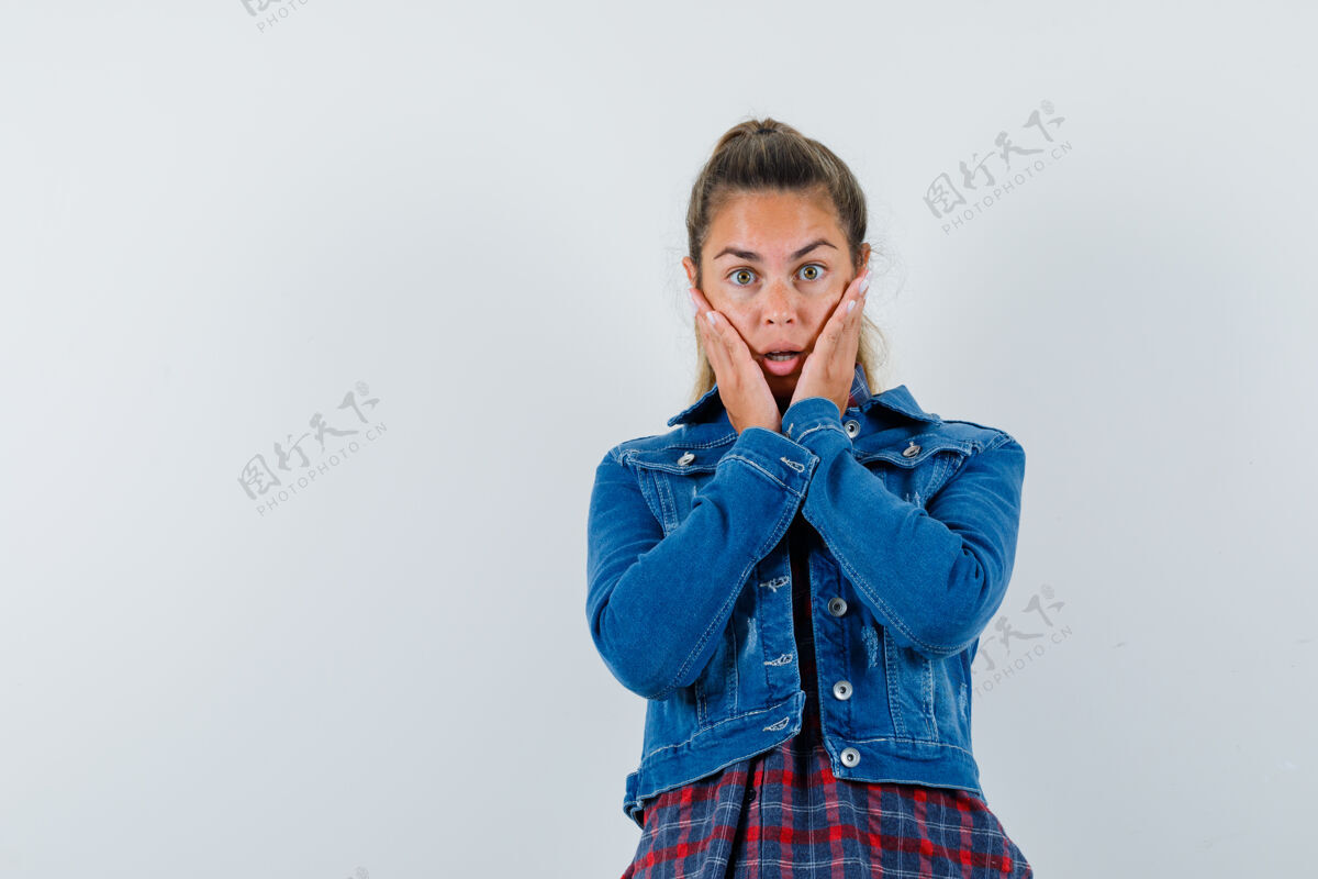 一个年轻女子手拉着面颊 穿着衬衫 夹克 看上去很惊讶 前视图年轻人手衬衫