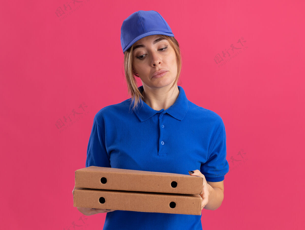 年轻给人印象深刻的年轻漂亮的送货女孩在制服举行和比萨饼盒看粉红色盒子姿势印象