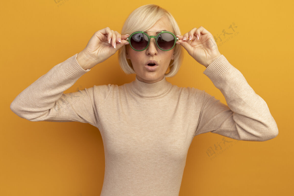 漂亮震惊美丽的金发斯拉夫女人看着相机透过太阳眼镜在橙色通过眼镜时尚
