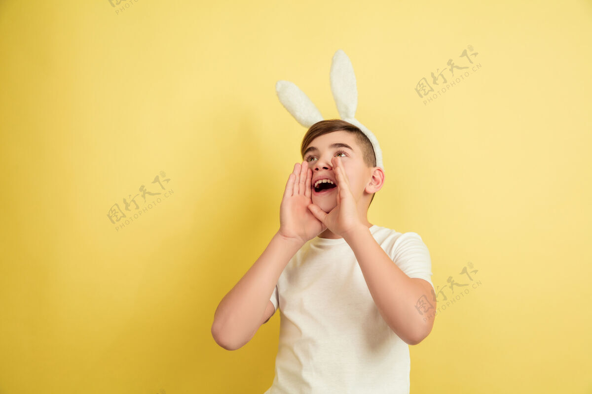 黄色白人男孩作为一个复活节兔子在黄色的工作室背景复活节快乐的问候狩猎春天男性