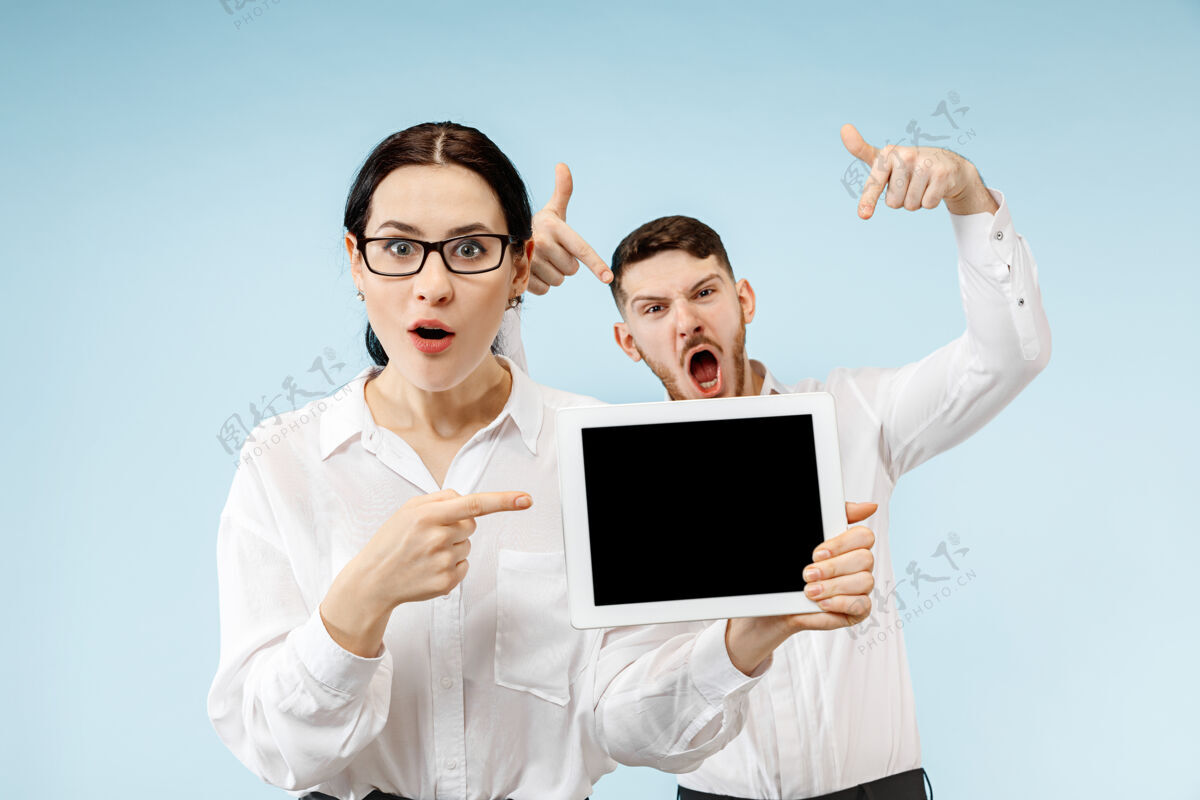 伙伴关系在蓝色工作室背景上 惊讶的商务男女微笑着 展示着笔记本电脑或平板电脑的空屏幕站立男性表演