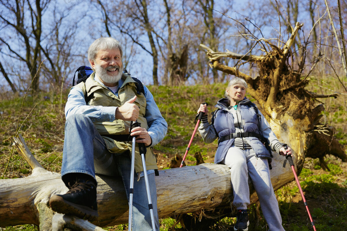 享受一起休息一对穿着旅游服装的老年夫妇在阳光明媚的日子里走在树旁的绿色草坪上旅游理念 健康的生活方式 放松和团聚活跃老年人自然