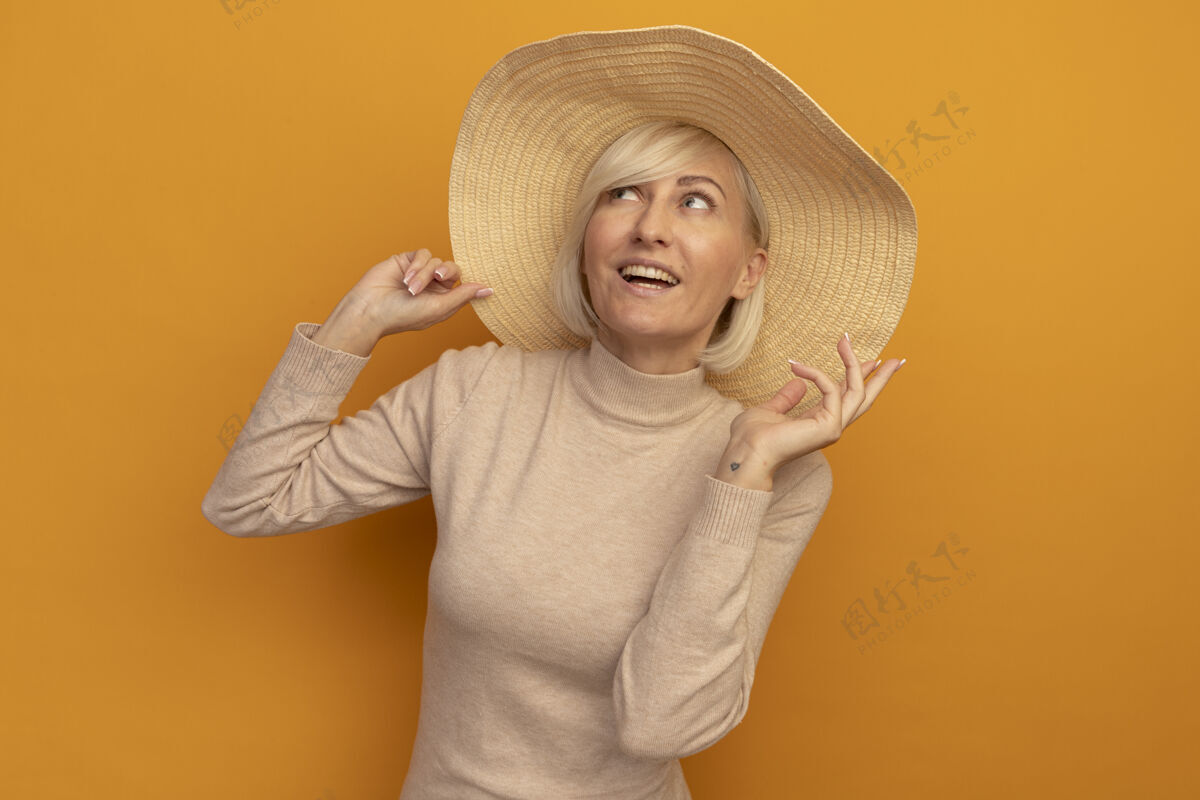 海滩面带微笑的金发斯拉夫女人 头戴沙滩帽 举手仰望橙色提高姿势斯拉夫