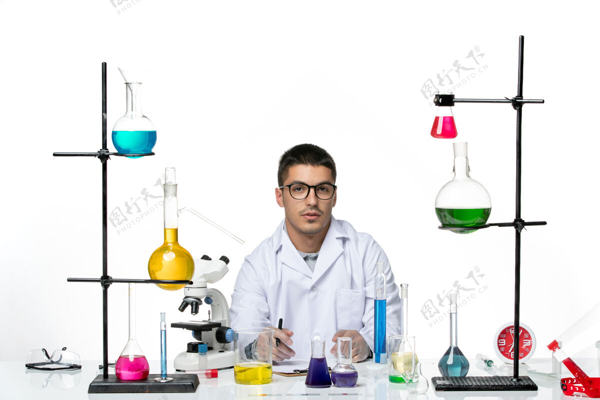 外套正面图身着医疗服的男性化学家坐在白色背景上写笔记病毒冠状病毒飞溅疾病科学实验室外套医学视图