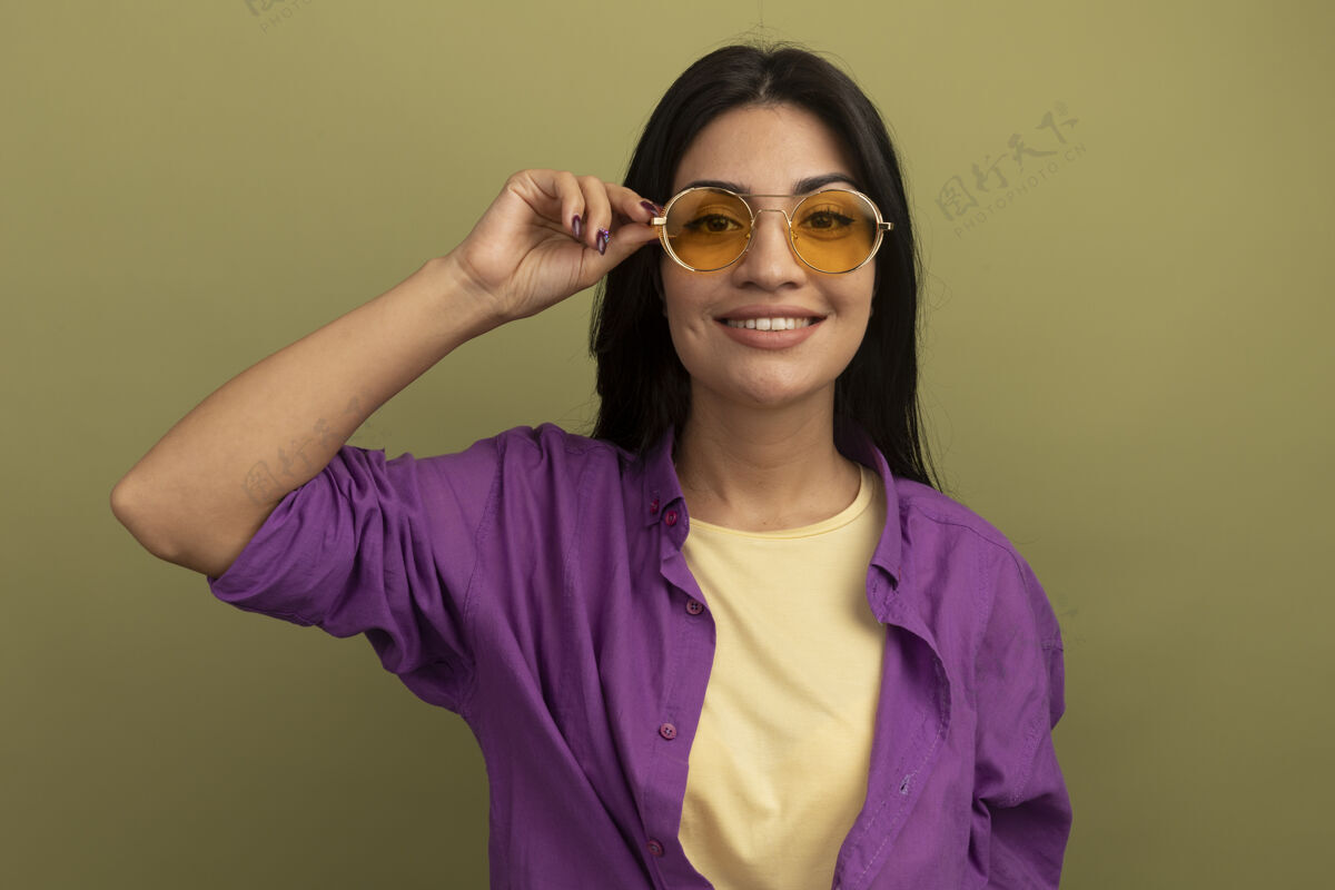 成人戴着太阳眼镜的黑发白人女孩微笑着看着橄榄绿的相机漂亮橄榄眼镜