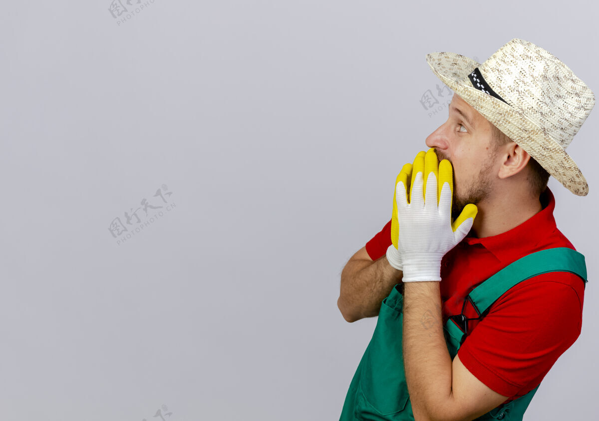 手套年轻英俊的斯拉夫园丁穿着制服 戴着帽子 戴着园丁手套 站在侧视图上 手放在嘴上 看起来很孤立穿人视图