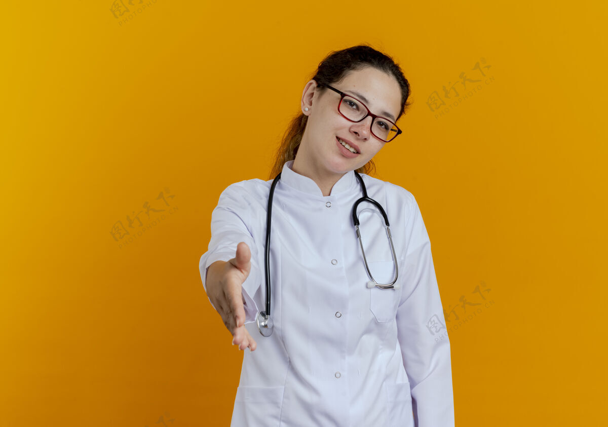 眼镜面带微笑的年轻女医生 穿着医用长袍 戴着听诊器 戴着眼镜 伸出手来女人微笑医学