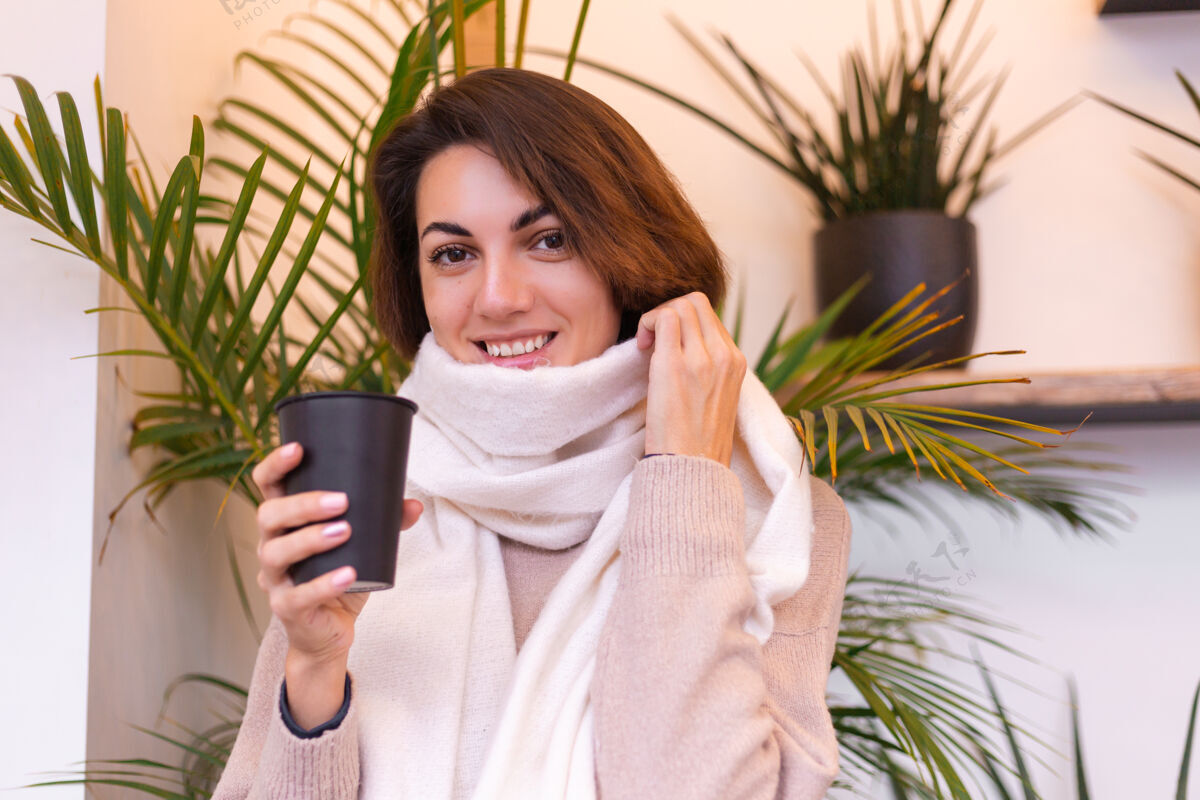 冬天一个女孩在舒适的咖啡馆里用一杯热咖啡取暖时尚年轻微笑
