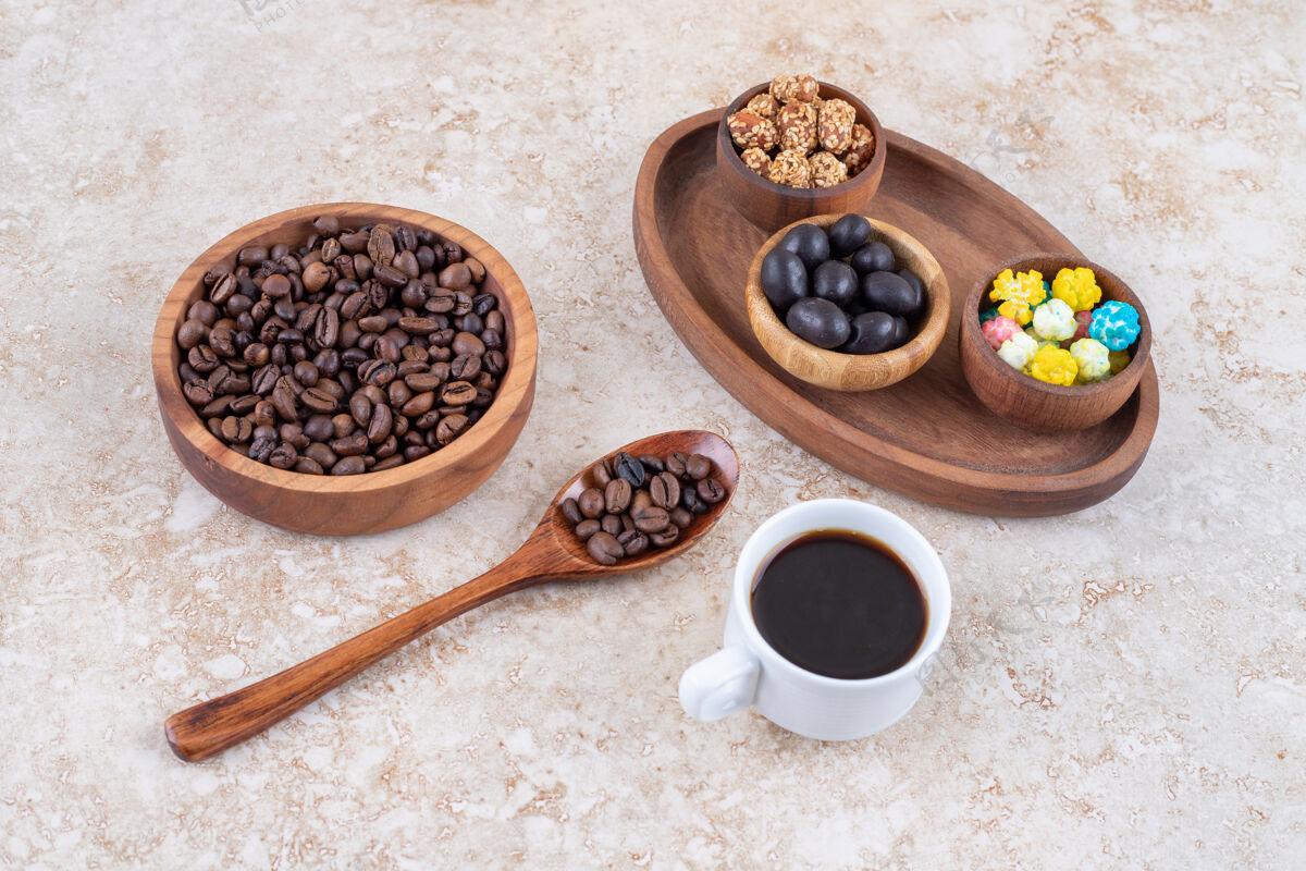 豆子在咖啡豆和一杯煮好的咖啡旁边的一个木制托盘里放各种小吃釉面杯子芳香