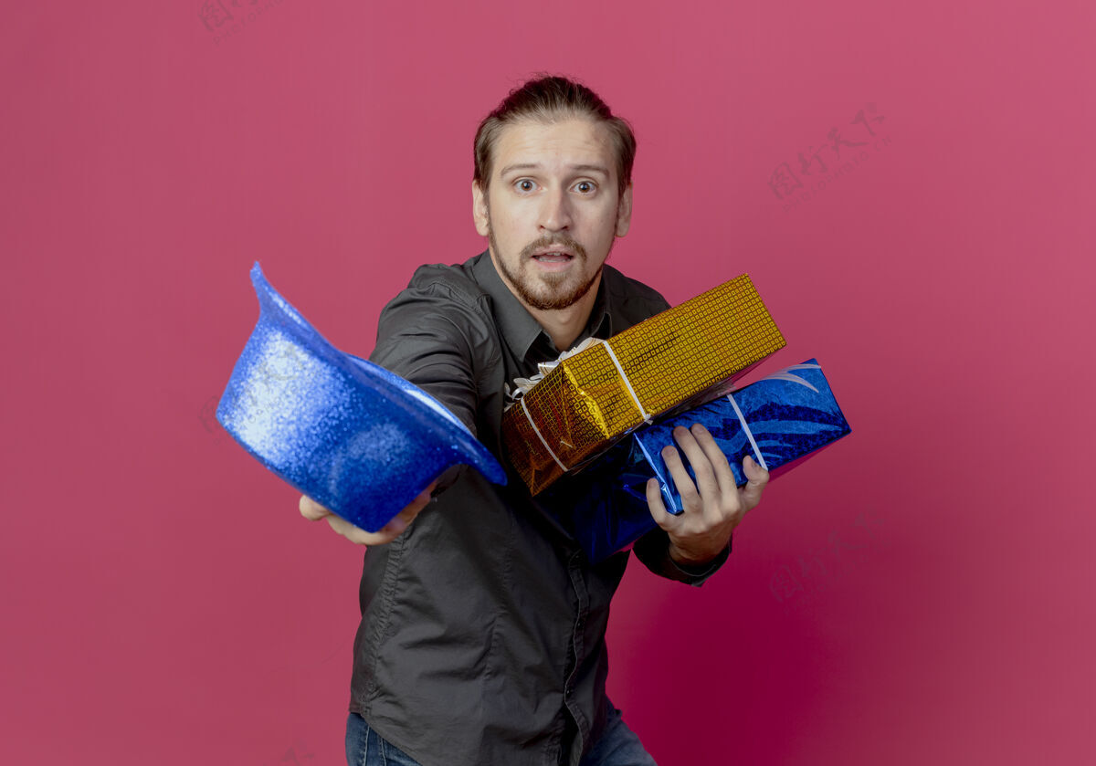 盒子焦急的帅哥站在一旁 手里拿着礼盒和蓝色帽子 孤立地贴在粉红色的墙上礼物抱着侧身